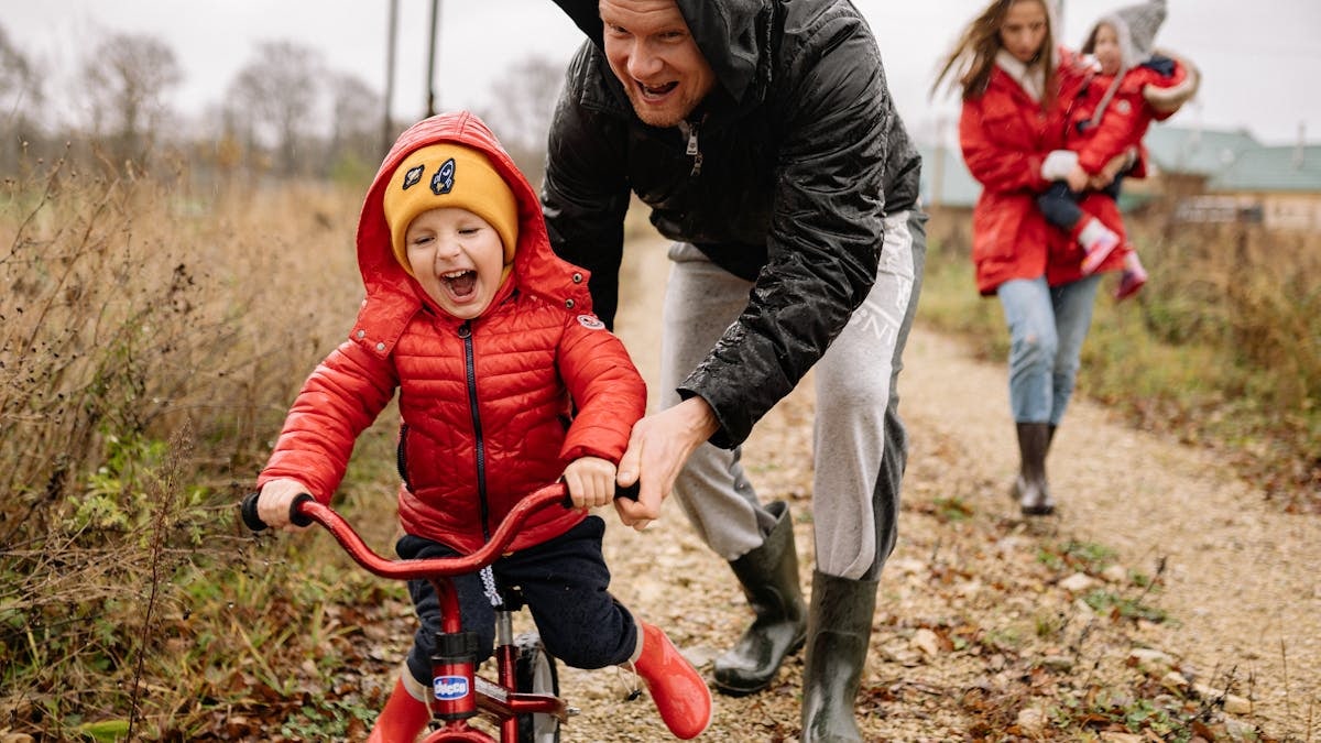 Father helping son ride a bicycle on a fall day while mother and daughter watch.