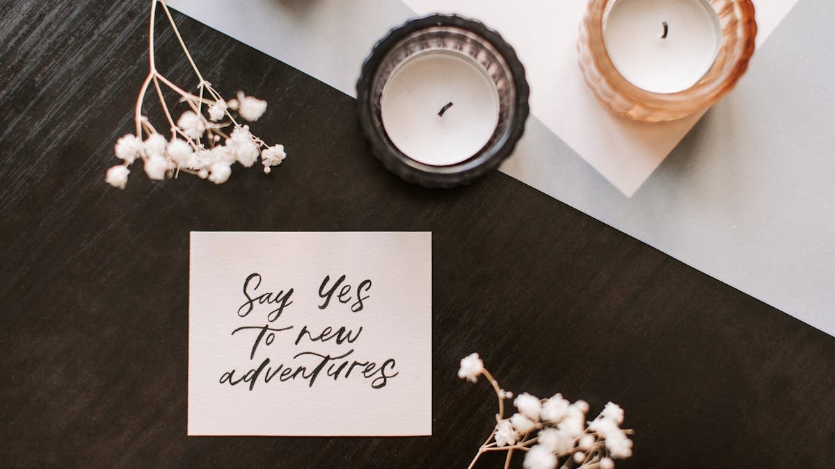 Flat lay of a motivational note with candles and flowers on a wooden surface.